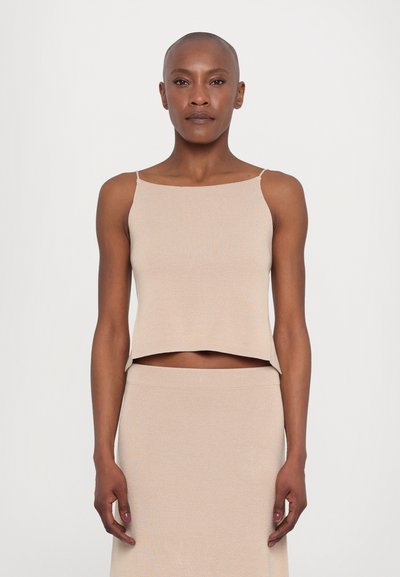 Hellbeige, verkürztes Tanktop mit dünnen Trägern und einem strukturierten Stoff. Kombiniert mit einem passenden, figurbetonten Rock, der ein minimalistisches Design betont.
