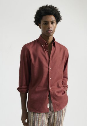Camisa de botones color burdeos hecha de tejido ligero, con cuello, mangas largas y puños enrollados. Etiqueta destacada en el lateral.