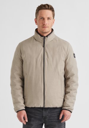 Helle beige, gesteppte Jacke mit hohem Kragen, Frontreißverschluss und schwarzen Akzenten. Verfügt über Seitentaschen und eine strukturierte Oberfläche.