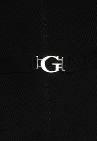 Mustaa kangasta, jossa on uritettu tekstuuri, ja hopeinen metallinen vyösolki, joka on muotoiltu kirjaimen "G" mukaan. Suunnittelussa korostuu minimalismi.