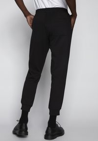 Pantalones deportivos negros con corte ajustado, cinturilla elástica y puños acanalados. Cuenta con un bolsillo trasero y está fabricado con una tela suave y ligera.