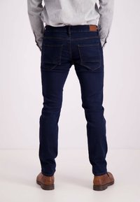 Granatowe dżinsy o slim fit, z dwiema tylnymi kieszeniami i brązową skórzaną metką na tylnej części pasa. W połączeniu z brązowymi skórzanymi butami.
