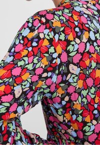 Kukkapainettu mekko, jossa musta tausta ja kirkkaita punaisen, pinkin, oranssin ja vihreän sävyjä. Kevyt kangas, jossa teksturoitu pinta.