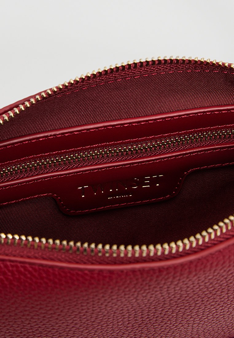 Interno di una borsa in pelle rossa con texture, dotato di una zip dorata, con foderatura in tessuto liscio e un'etichetta del marchio impressa su una patella in pelle.