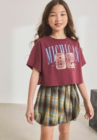 Bordeaux kleurige cropped t-shirt met de print "MICHIGAN 82" in blauw en een geruit ontwerp. Gecombineerd met een gele, blauwe en bruine geruite schouderrok.