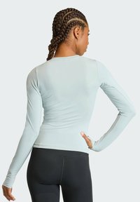 Haut de sport à manches longues bleu clair en tissu lisse et extensible, associé à un legging noir. Coupe ajustée sans logos visibles.