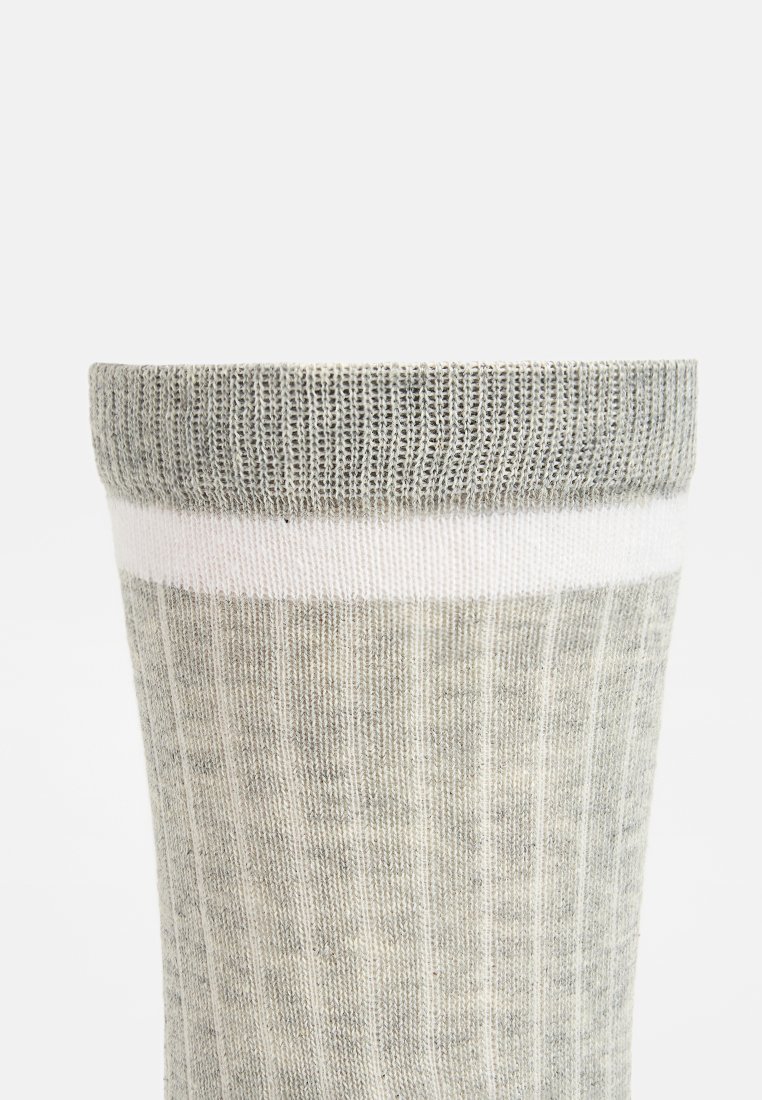 Calcetín gris de punto con una textura acanalada y una banda blanca en la parte superior. El calcetín presenta un patrón sutil y una forma cilíndrica.