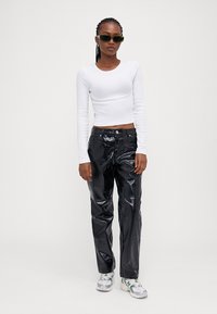 White long-sleeve top and black patent leather pants. Black sunglasses, relaxed fit, with a glossy texture and mock pockets. Neutral sneakers.
