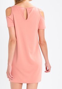 Jasnoróżowa sukienka z miękkiego materiału, z wycięciami na ramionach i małym otworem z tyłu, zaprojektowana z krótkimi rękawami.