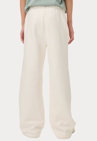 Losse, crèmekleurige sweatpants met een elastische tailleband en een gladde textuur, voorzien van wijde benen en een minimalistisch ontwerp.