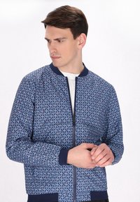 Marineblaue Bomberjacke mit floralem Muster in Blau und Weiß, mit ribbeltem Kragen, Reißverschluss und elastischen Bündchen.