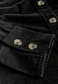 Gros plan sur un tissu en velours côtelé noir avec deux boutons marbrés beige sur le poignet d'une manche et des boutons supplémentaires sur le corps.