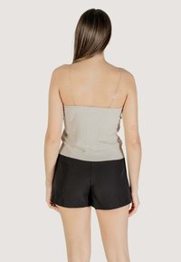 Top grigio chiaro a costine con spalline sottili simili a catene, abbinato a pantaloni corti neri. Texture liscia con un design aderente, che mostra accentuazioni minime.