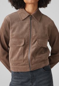 Brown corduroy jacket with a collared neckline, zip closure, and two front pockets. Short, relaxed fit with vertical ribbed texture.