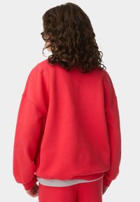 Sudadera roja con un corte relajado, que presenta mangas largas, puños de canalé y un cuello redondo. Fabricada en una tela suave y lisa con un diseño ligeramente oversize.