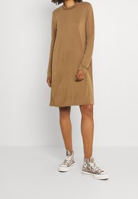 Långärmad, beige klänning med avslappnad passform, gjord av mjukt material. Kombinerad med högstövlar med ett svart och vitt zebramönster.