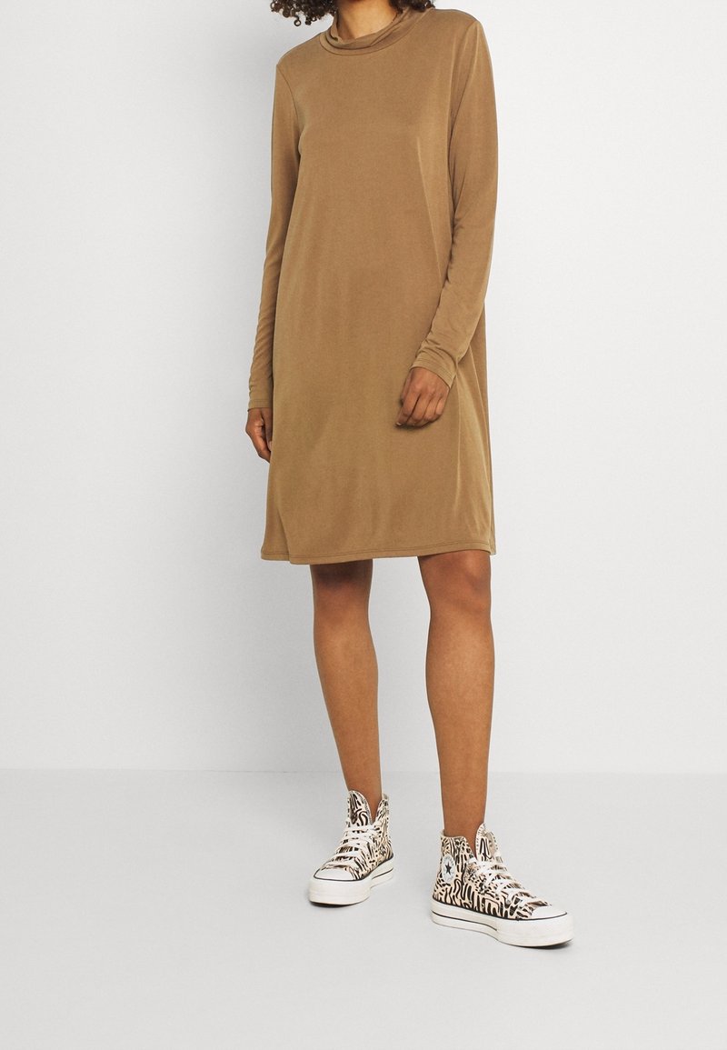 Långärmad, beige klänning med avslappnad passform, gjord av mjukt material. Kombinerad med högstövlar med ett svart och vitt zebramönster.