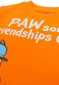 T-shirt en coton orange avec un personnage de dessin animé et le texte "Des amitiés super". Le tissu a une texture lisse et des manches courtes.