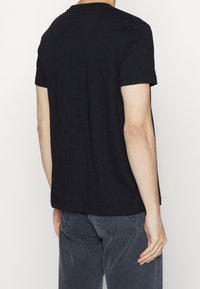 Černé tričko s krátkým rukávem vyrobené z bavlny, s kulatým výstřihem a rovný střih. Zadní pohled ukazuje jednoduchý design bez vzorů.