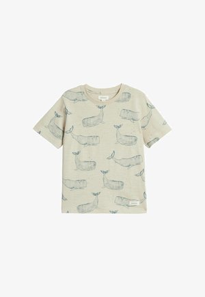 Beżowy t-shirt dla malucha z krótkim rękawem z niebieskimi ilustracjami wielorybów na całej powierzchni i małą materiałową metką z logo w pobliżu brzegu.
