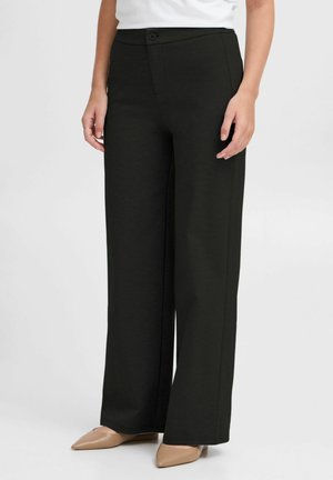 Wide-leg black pants made of textured fabric, featuring a front button closure and pockets, paired with beige pointed-toe shoes.