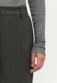 Haut gris à manches longues avec une texture, équipé de poignets ajustés, associé à un pantalon droit gris foncé au fini lisse et avec des passants de ceinture.