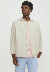 Light beige oversized shirt with a button-down front, single chest pocket, and long sleeves layered over a light pink t-shirt.