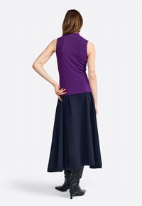 Haut sans manches violet avec une finition texturée, associé à une longue jupe bleu marine et des bottes noires jusqu'aux genoux, vue de dos.