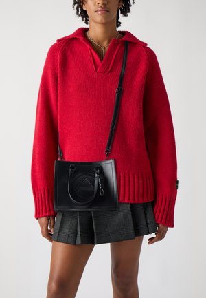Suéter grueso de punto rojo con escote en V y bordes acanalados, combinado con un bolso de cuero negro con un diseño de triángulo en relieve y asas cortas.