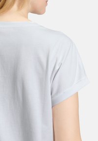 Světle šedé bavlněné tričko s ohrnutými krátkými rukávy, s jemnou strukturou a volným střihem, viděné z dohledu zezadu.