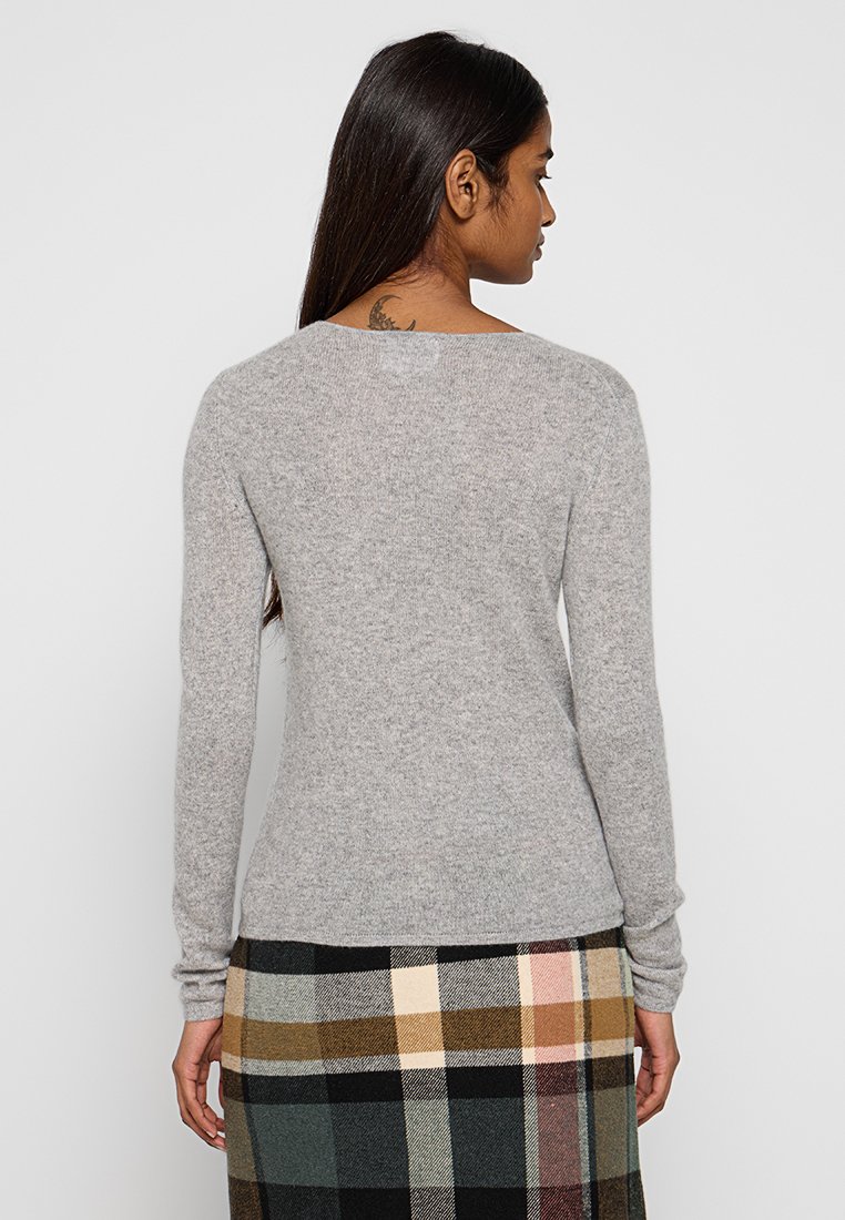 Maglione grigio a maniche lunghe in morbido tessuto a maglia con scollatura rotonda. Indossato con una gonna a quadri con tonalità beige, verde e nera.