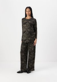 Løveprint loungewear-sett i svart og tan, med langermet topp og vide bukser laget av myk, lett stoff.