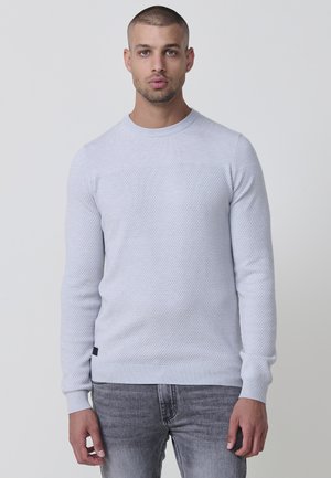 Suéter de punto gris claro con patrón texturizado, cuello redondo y puños y dobladillo acanalados. Llevado con jeans grises.