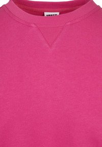 Gros plan d'un sweat-shirt rose vif à col rond avec un col côtelé et un détail côtelé triangulaire sous l'encolure.