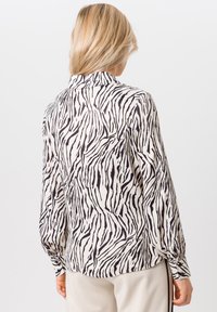 Blouse à manches longues en tissu léger, présentant un motif rayé zèbre noir et blanc, avec un col et une coupe décontractée.