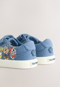 Kék gyermek sportcipők a Paw Patrol karaktereivel az oldalukon, fehér talpakkal és tappancsnyomokkal a sarkon.