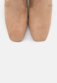 Bottines en suède beige avec un bout pointu et une semelle noire plate. Texture lisse et design minimaliste sans quincaillerie ou accents visibles.