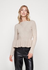 Maglione beige lavorato a maglia con texture a costine, orlo a peplum, maniche lunghe e scollatura rotonda, abbinato a pantaloni in pelle nera.