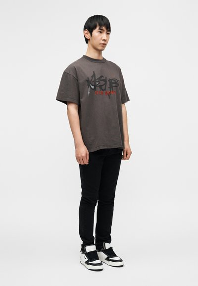 Γκρι υπερμεγέθη μπλουζάκι με μαύρο και κόκκινο γραφικό κείμενο «NEW YORK», συνδυασμένο με μαύρο στενό τζιν και ασπρόμαυρα αθλητικά παπούτσια.