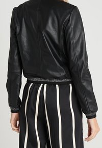 Czarna skórzana kurtka z dopasowanym krojem, ściągaczami na rękawach i teksturowanym wykończeniem u dołu, zestawiona z czarno-białymi spodniami w paski.