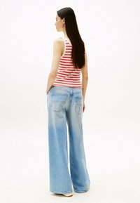 Top de tirantes a rayas rojo y blanco combinado con unos vaqueros anchos de tiro alto en azul claro, que cuentan con bolsillos traseros y un corte relajado. Textura suave en general.