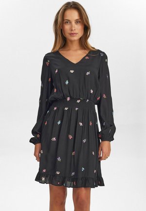 Robe noire à manches longues, décolleté en V et taille élastique. Présente une broderie florale colorée et un ourlet à volants pour le détail.