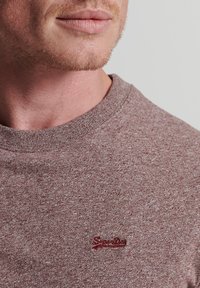 Bordowy sweatshirt z okrągłym dekoltem, wykonany z teksturowanej tkaniny, z małym, czerwonym, haftowanym logo na piersi.