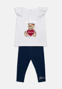 Top blanc à manches courtes avec manches à volants ornées d'un motif d'ours en peluche tenant un cœur rouge. Leggings bleu marine avec détail logo.
