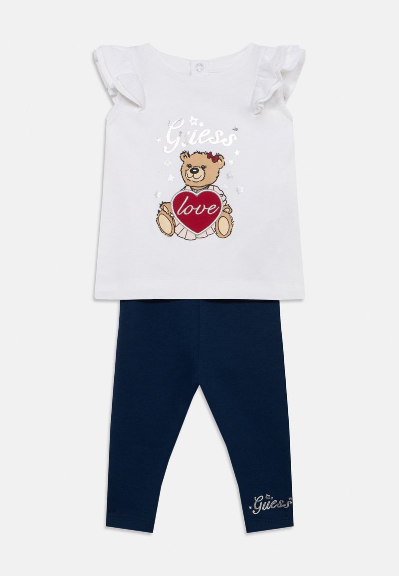 Top blanc à manches courtes avec manches à volants ornées d'un motif d'ours en peluche tenant un cœur rouge. Leggings bleu marine avec détail logo.