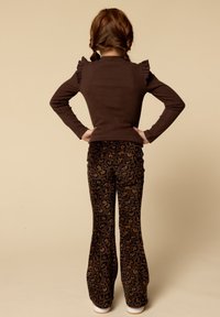 Bruine lange mouwtop met gerimpelde schouders, gecombineerd met donkerbruine flared broek met een luipaardprint. Witte sneakers worden gedragen.