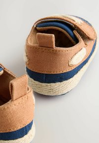 Chaussures en toile pour tout-petits de couleur beige et marine, avec une bande texturée bleue, une semelle tissée plate et des sangles Velcro réglables.