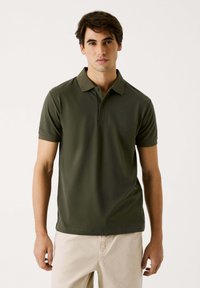 M�ørkegrøn polo-shirt lavet af glat stof, med en klassisk krave og korte ærmer, samt et diskret logo på brystet.