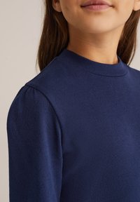 Tumši zila adīta džemperis ar augstu apkakli un pūkainām piedurknēm, ar neuzkrītošu sirds rakstu un gludu tekstūru.