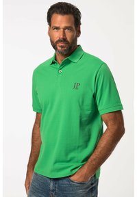 Grøn polo skjorte i bomuld med klassiskkrave. Har et lille maroon logo "JP 1880" på brystet. Korte ærmer, lige kant.